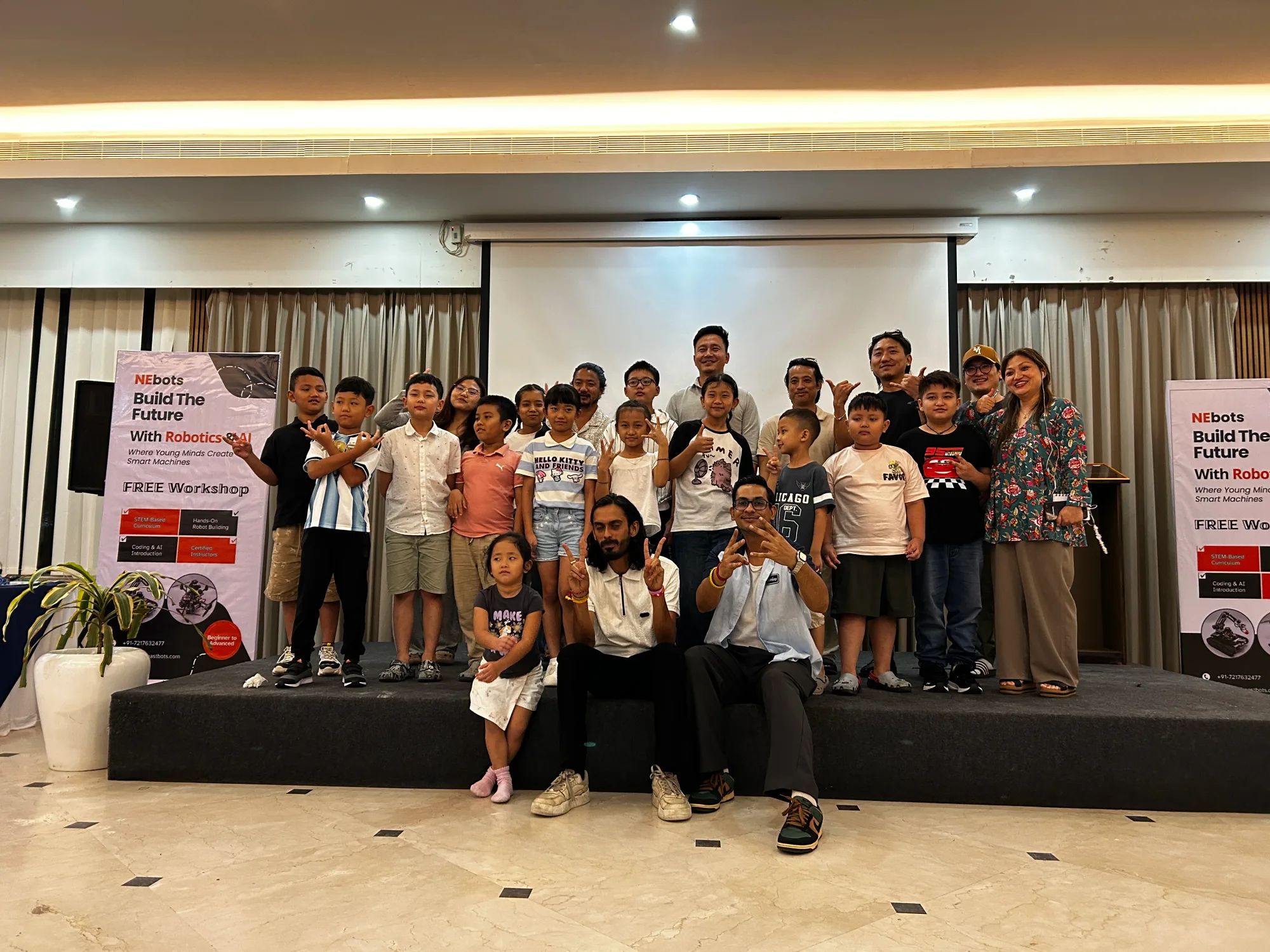 Group photograph of students, parents and the NEbots team on stage at the free robotics and AI workshop in Itanagar